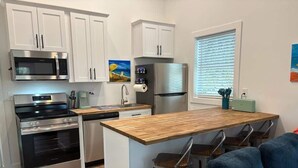 A compact kitchen with a central island, stainless steel appliances, and a blue upholstered sofa. - 120 Falkirk Small Pet Friendly Cottage near Beach (Fort Myers Beach)