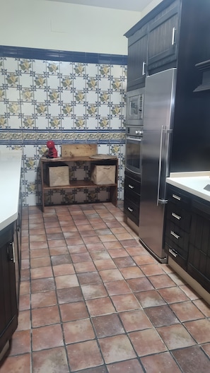 A kitchen with tiled backsplash, a wooden shelf, a refrigerator, and cabinets. - Country House 'Casa Rural Valle' with Mountain View, Private Pool and Air Conditioning (La puebla de los infantes)
