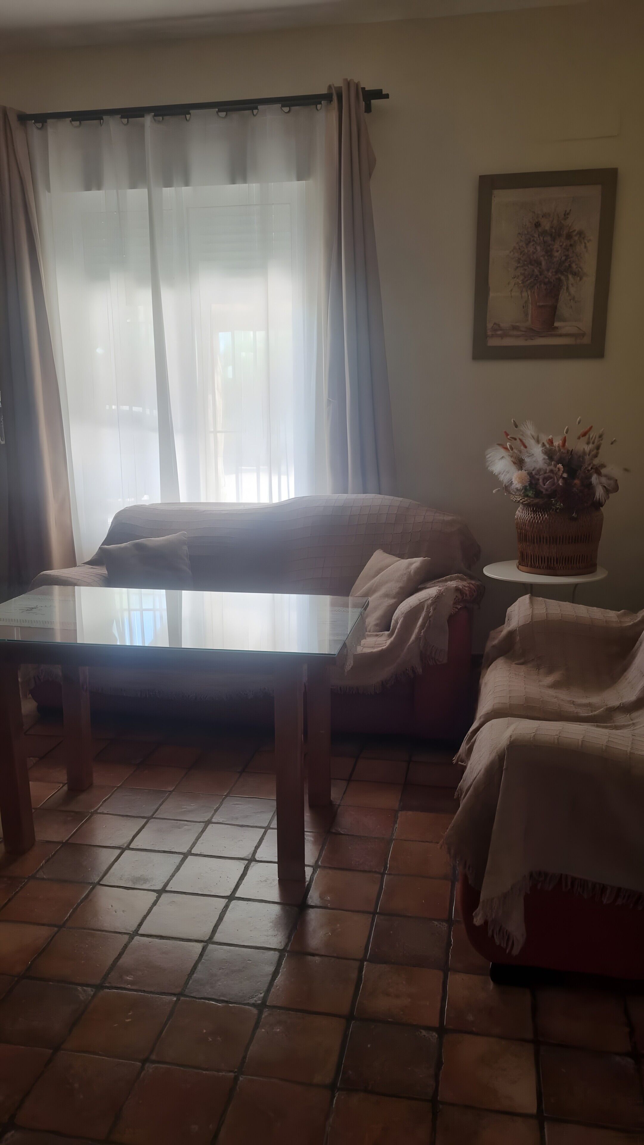 Un soggiorno con un divano, un tavolino in vetro, un tavolino in vimini con un vaso e un pavimento piastrellato.