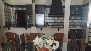 A dining table with a glass top and wooden chairs, a kitchen in the background, and a decorative basket with flowers. - Country House 'Casa Rural Valle' with Mountain View, Private Pool and Air Conditioning (La puebla de los infantes)