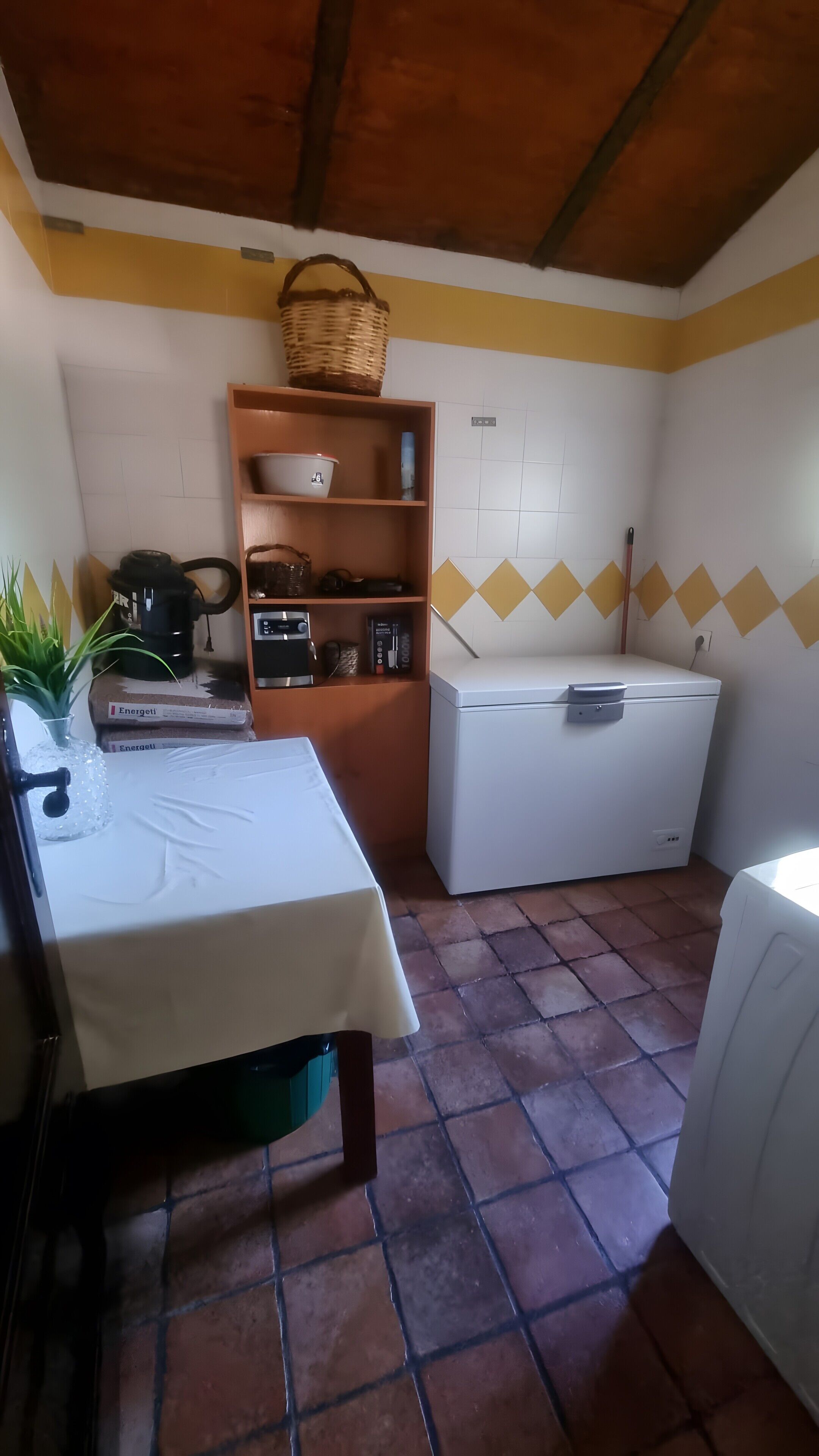 Una cocina con una mesa, estanterías, una lavadora y suelo de baldosas.