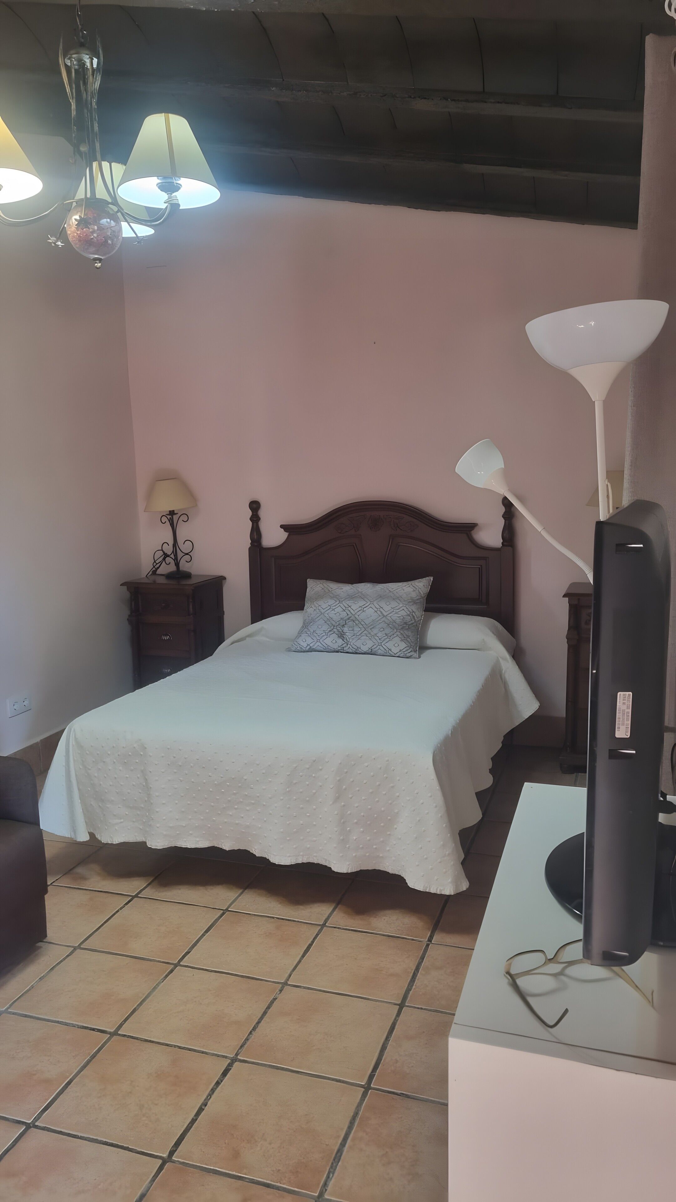 Een slaapkamer met een bed, nachtkastje, lamp en televisie.