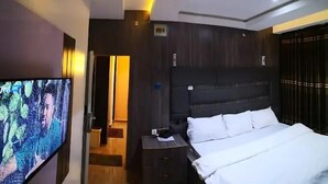 Ein modernes Hotelzimmer mit einem großen Bett, einem Flachbildfernseher und einem dunklen Holz-Kopfteil.