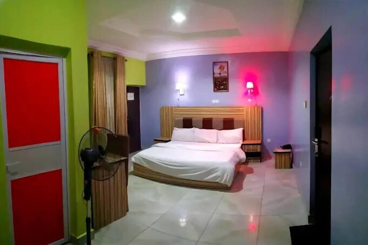 A bedroom with a bed, a bedside table, a lamp, and a wall-mounted light fixture.