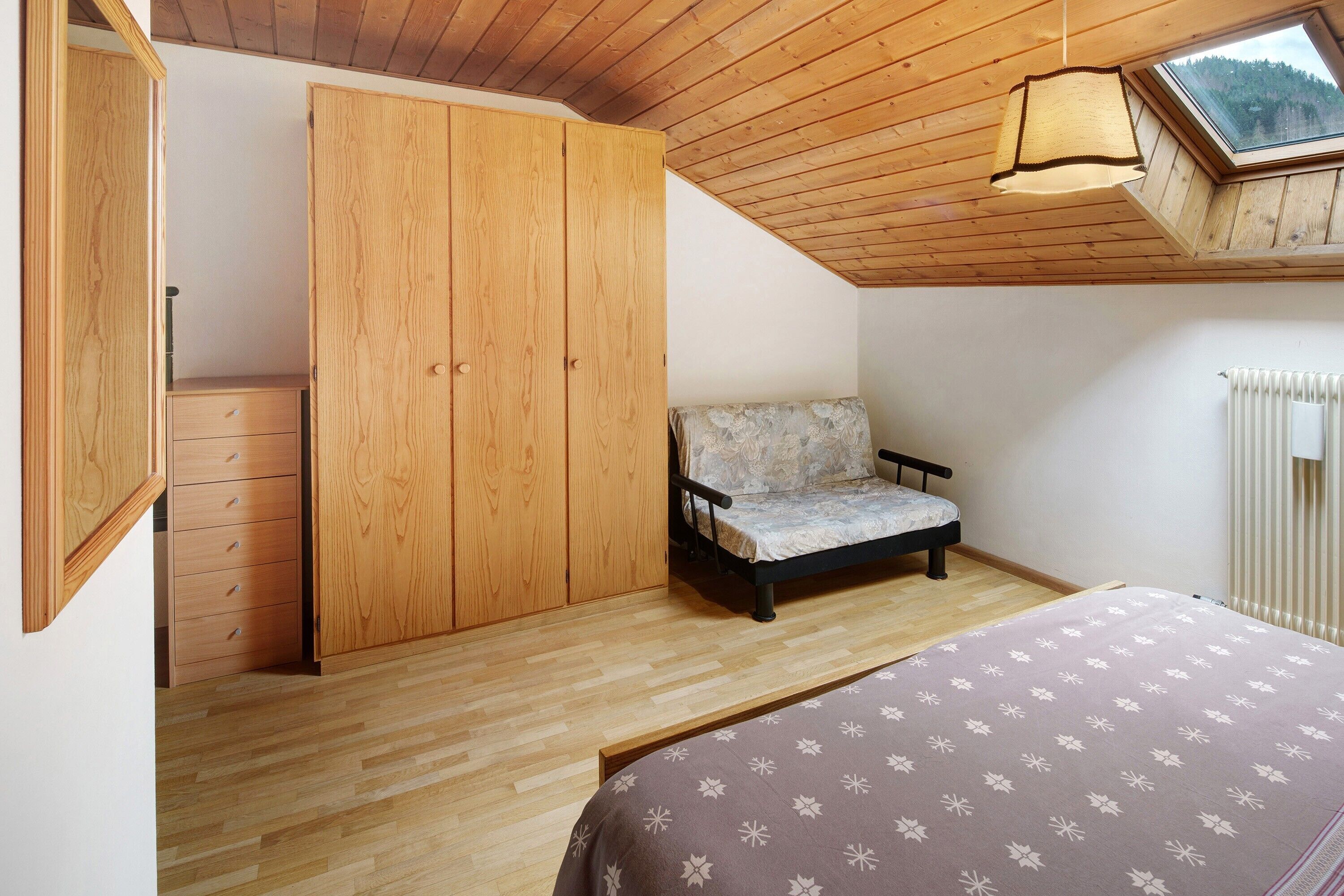 A bedroom with a wooden ceiling, a bed, a sofa, a wardrobe, and a skylight.