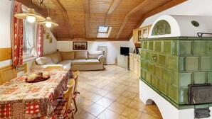A cozy room with a wooden ceiling, a dining table with a checkered tablecloth, a sofa, and a green cabinet.