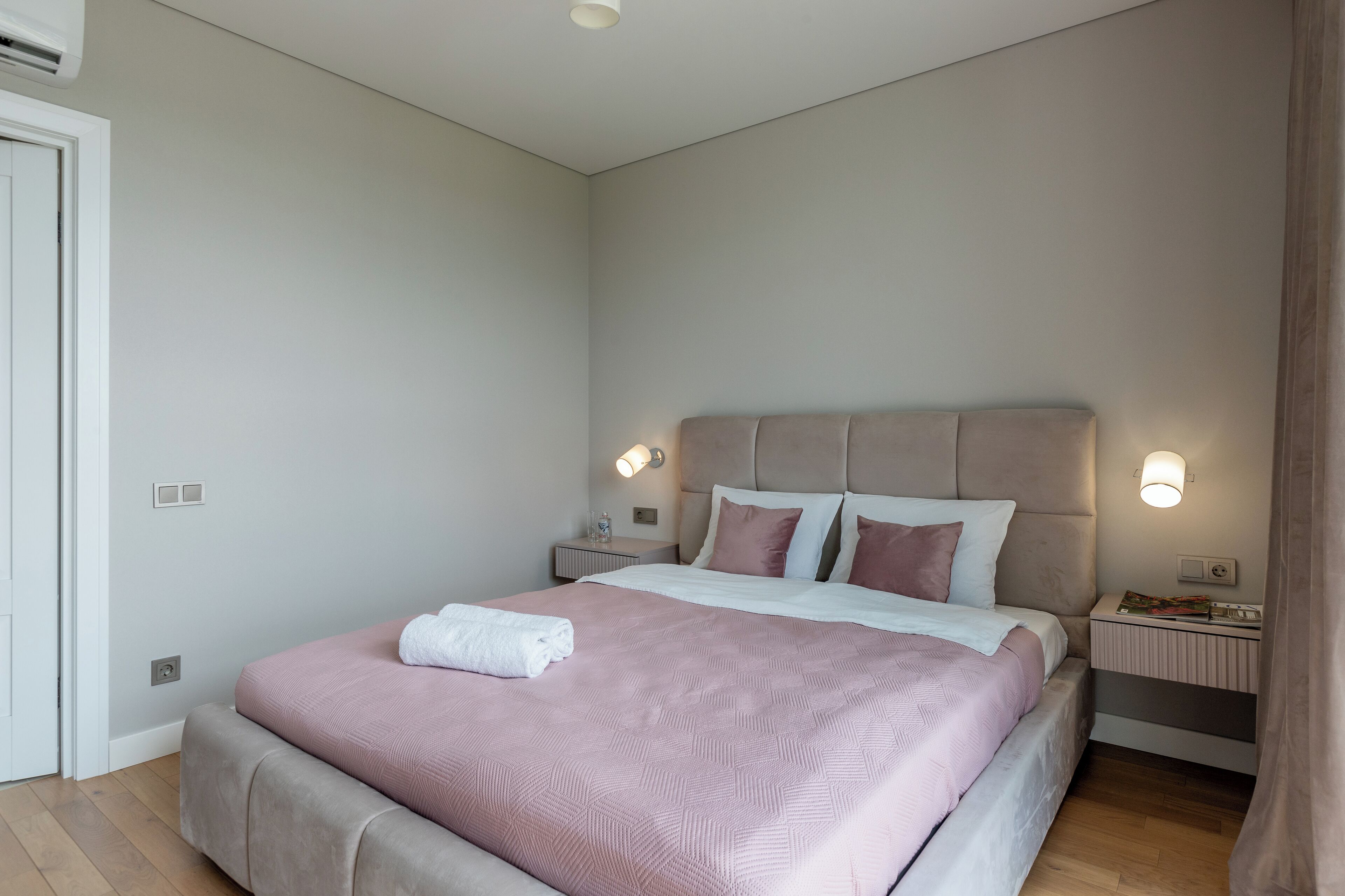 A neatly made bed with a pink and white bedspread, two bedside tables with lamps, and a door on the left.