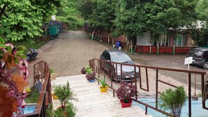 A courtyard with a car parked on a paved area, surrounded by greenery and a metal railing. - sky ganga resort (Rishikesh)