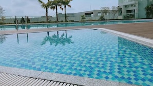 Una piscina con un estampado de baldosas a cuadros, rodeada por una terraza de madera y palmeras.