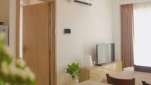 Una habitación de hotel con cama, escritorio, televisor, aire acondicionado, planta y ventana con cortinas.