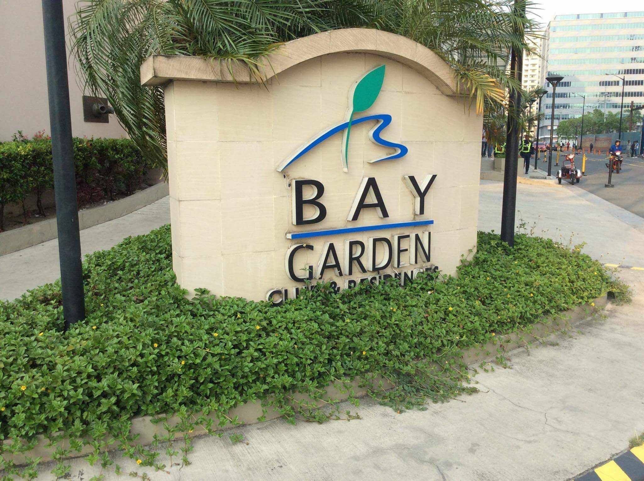 Une enseigne indiquant « Bay Garden », avec un logo, entourée de verdure et bordée d’un trottoir.