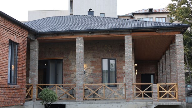 A two-story building with a brick facade, large windows, and a covered porch with wooden railings.