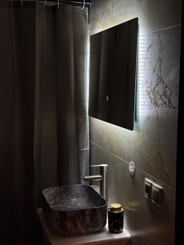 A modern bathroom with a marble sink, a large mirror, and a shower curtain.