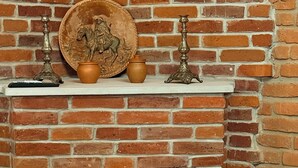 A brick fireplace with a decorative plate, two candles, and a wicker chair.