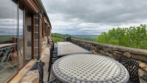 Um pátio com mesa redonda e cadeiras, um muro de pedra e vista para o campo.
