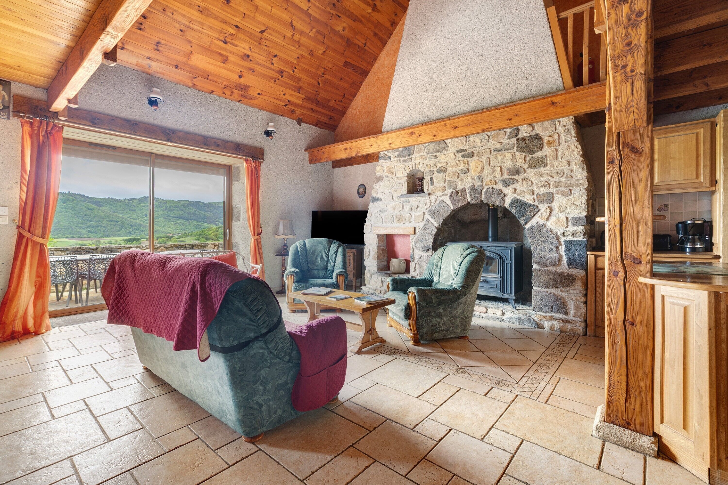 Una sala de estar acogedora con chimenea de piedra, vigas de madera en el techo y vistas al exterior.