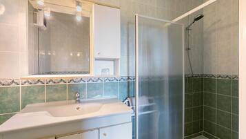 Un baño con lavamanos blanco, un espejo, ducha con puerta de vidrio y paredes con azulejos verdes.