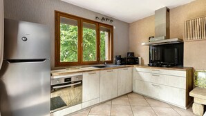 Eine moderne Küche mit Edelstahl-Kühlschrank, integriertem Backofen, Mikrowelle und einem großen Fenster mit Blick auf Grünflächen.