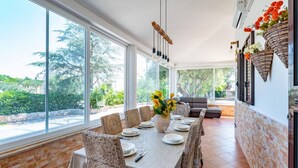 A dining area with a table set for six, large windows, and a view of greenery outside. - Villa Rita Ostuni with pool by Rentbeat  (Ostuni)