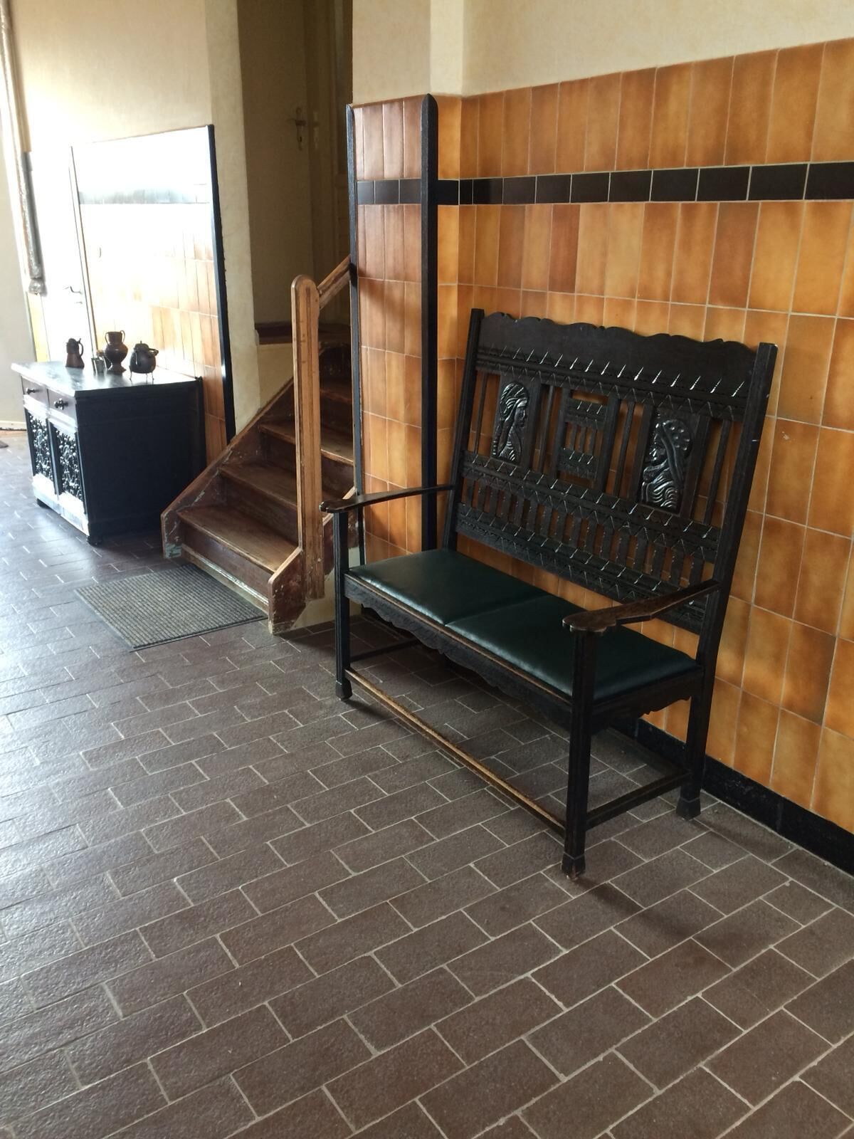 Un banco con respaldo decorado con un diseño tallado, ubicado frente a una pared con un patrón de azulejos.