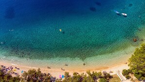 An aerial view of a beach with clear blue waters, a sandy shore, and a few boats.