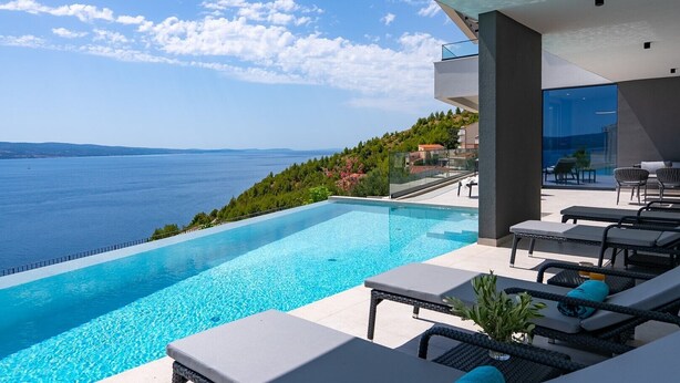 A modern infinity pool with a clear view of the sea and hills.