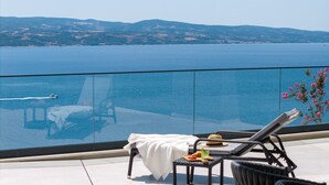 A balcony with a glass railing overlooking a body of water and distant hills.