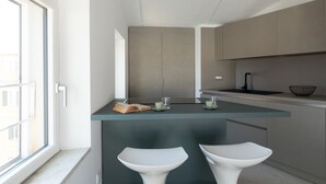 Eine moderne Küche mit einer zentralen Kochinsel, zwei Barhocker und Blick ins Freie.