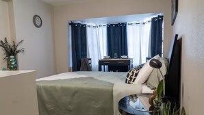 A bedroom with a bed, a desk, a chair, a clock, and a window with curtains. - Perfect Location! All include Tampa Private Suite (Tampa)