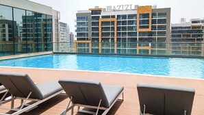 Une piscine sur le toit, avec des chaises longues, et un bâtiment portant l’inscription « AZIZI » en arrière-plan.