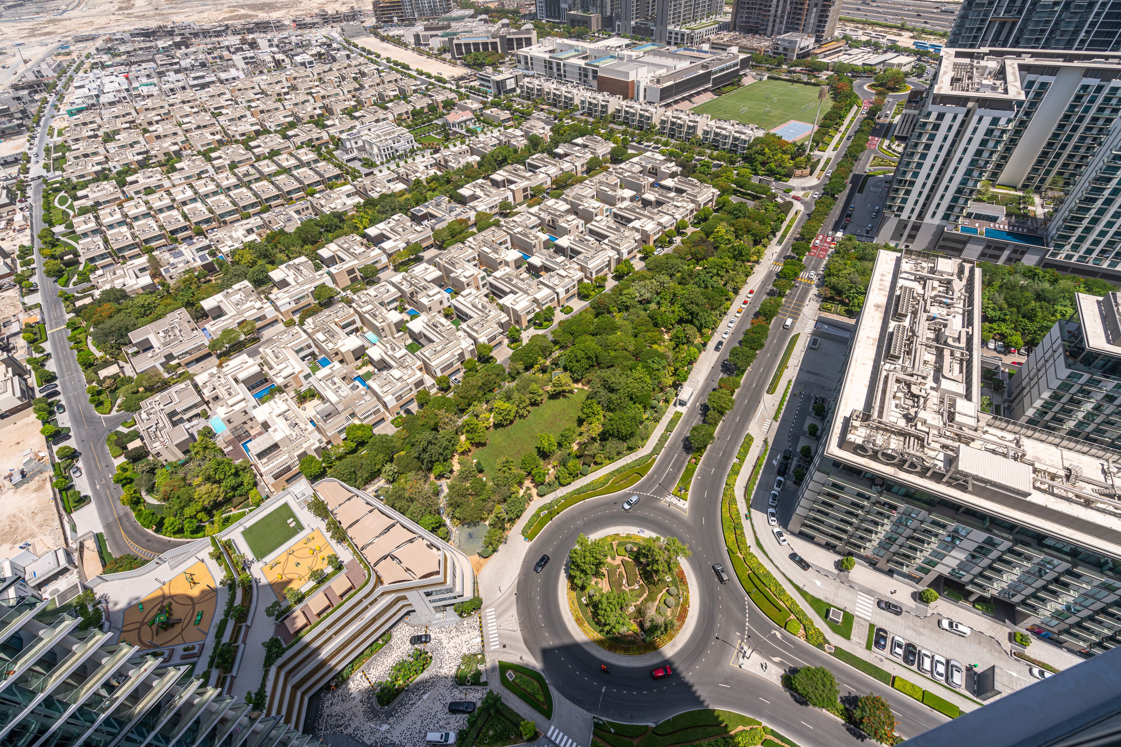 An aerial view of a modern urban area with a mix of high-rise buildings, green spaces, and a roundabout.