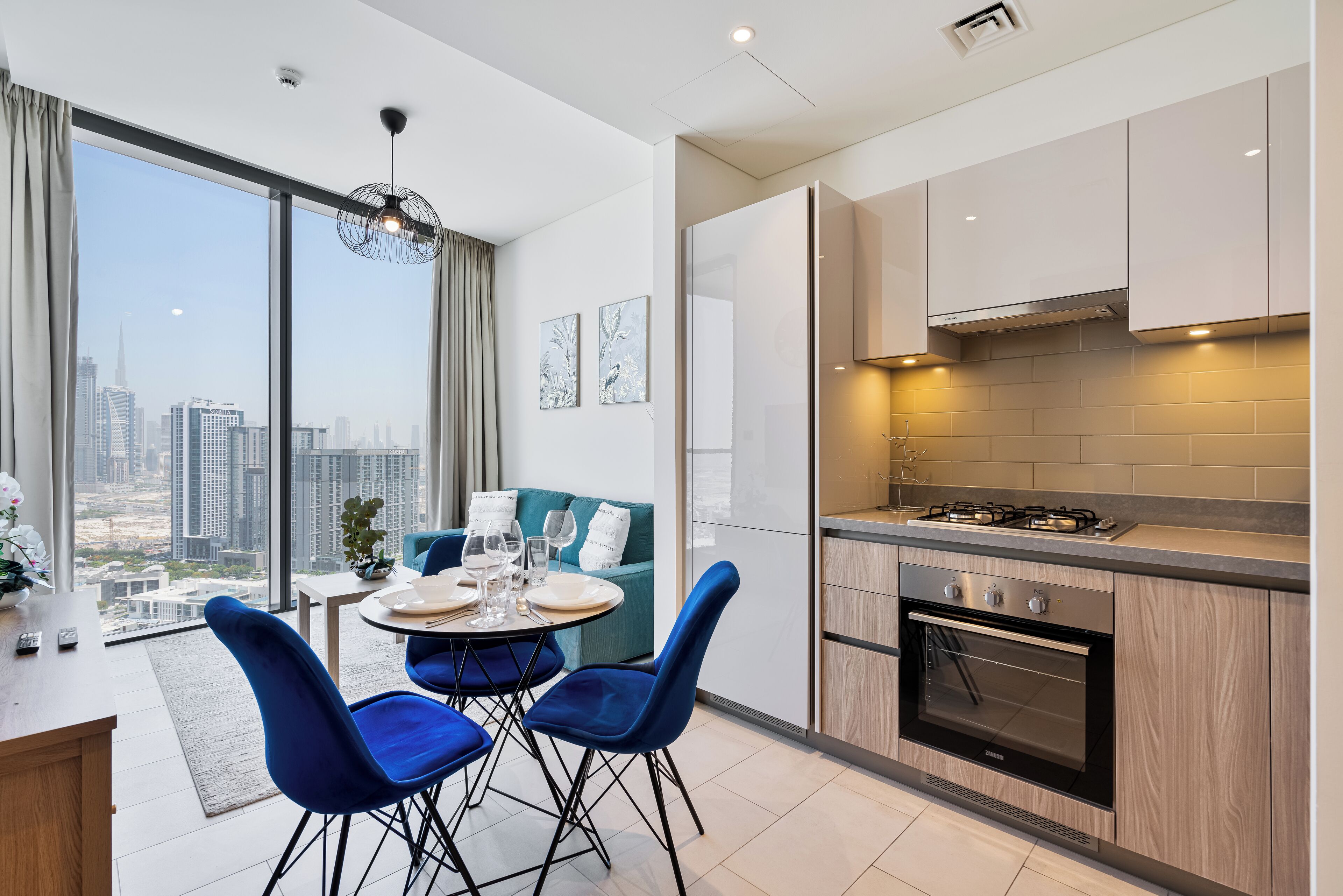 A modern kitchen with a large window, a dining area with blue chairs, and a city view.