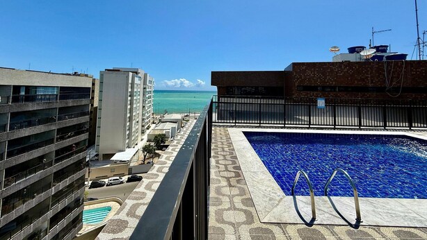 A rooftop pool with a view of the ocean, surrounded by buildings. - Edifício Santorini (Maceio)