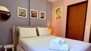 A neatly made bed with white linens and towels, a small bedside table, and a wall with framed pictures. - Edifício Santorini (Maceio)