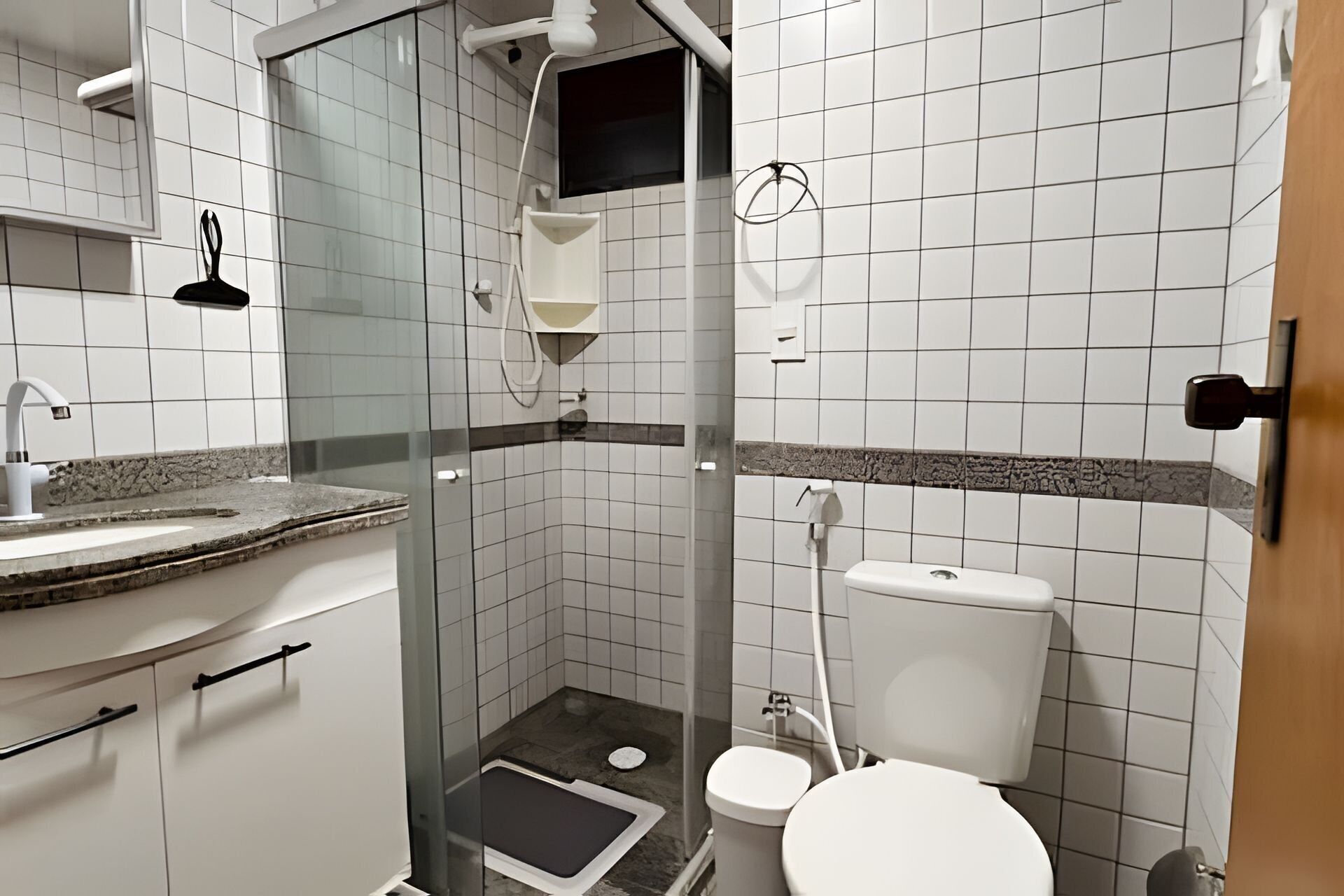 Un baño pequeño con azulejos, ducha, inodoro y lavamanos.