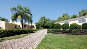 Ein gepflasterter Weg führt zu einem Gebäude mit einem Ziegeldach, umgeben von gepflegtem Rasen und Hecken.