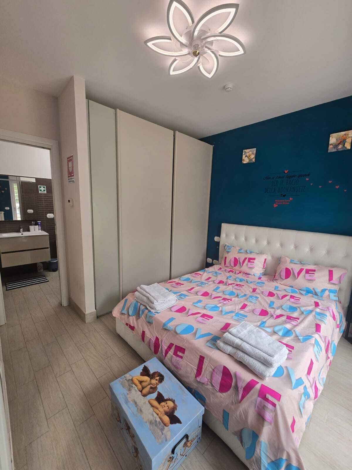A bedroom with a bed, a wardrobe, a vanity with a mirror, and a ceiling light fixture.