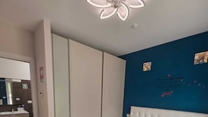 Et soveværelse med seng, garderobeskab, sminkebord med spejl og loftslampe.