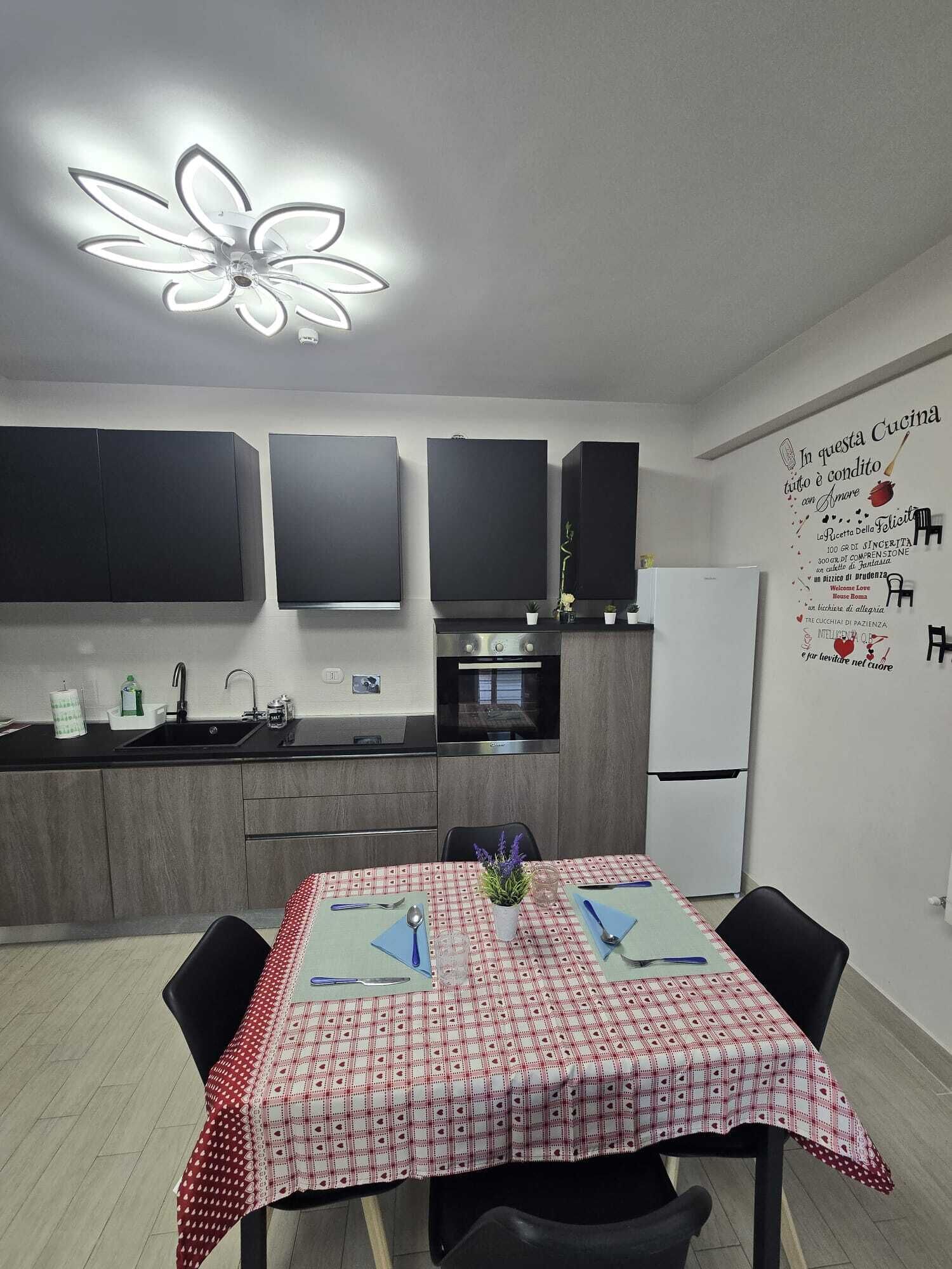 A modern kitchen with a dining area, featuring a table set for two with a red and white checkered tablecloth.