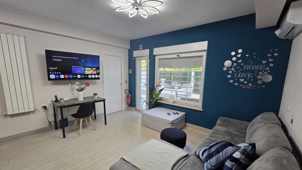 En moderne stue med en grå sofa, et lille bord med en vase, et fladskærms-tv og et vindue med udsigt udad.