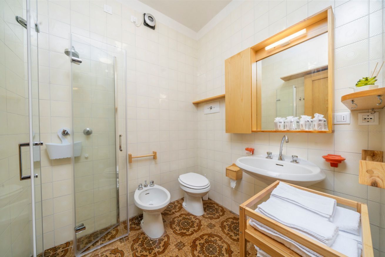 A bathroom with a glass shower enclosure, a bidet, a toilet, a sink, and a mirror.
