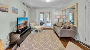 Un salon comprenant un téléviseur, un canapé, un fauteuil, un tapis et un grand miroir.
