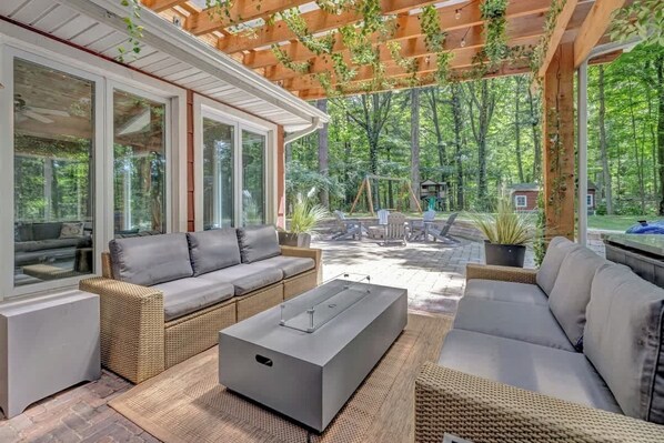 A covered patio with wicker furniture, a modern coffee table, and a view of a wooded area.