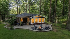 Une cabane dotée d’un foyer extérieur et de sièges, située dans un cadre boisé.