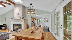 Un salon spacieux doté d’une cheminée, d’une table à manger en bois et de grandes fenêtres.
