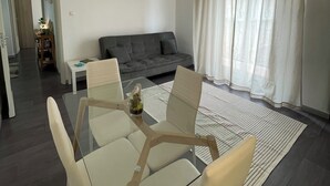 A modern living room with a glass dining table, white chairs, a grey sofa, and a large window with sheer curtains. - Cibali Metro Stay (Catania)