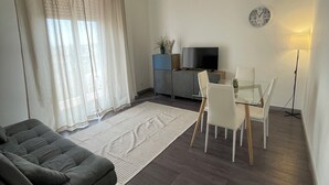 A modern living room with a sofa, a dining table with chairs, a TV, and a clock on the wall. - Cibali Metro Stay (Catania)