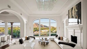 Un salon spacieux doté d’une grande fenêtre en arc de cercle, de canapés blancs, d’une cheminée et offrant une vue sur les montagnes.