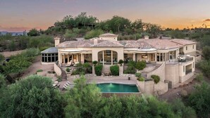 Une grande maison avec une piscine, entourée de verdure et de collines.