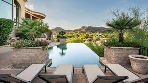 Une piscine avec des chaises longues, un jardinière en pierre et une vue sur les montagnes.
